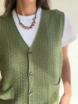 Chaleco de tejido de punto con textura, escote en V y cierre frontal con botones. Presenta dos bolsillos delanteros y terminaciones en tejido acanalado en el ruedo.