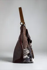 Cartera de cuero combinada con texturas y pelo natural con estampado animal print tipo vaca, diseño envolvente con líneas orgánicas, asa de hombro y bolsillos exteriores.