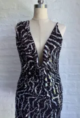 Vestido corto negro con lentejuelas plateadas dispuestas en un patrón ondulado o geométrico. Presenta un escote profundo en V pronunciado y tirantes finos tipo espagueti.
