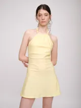 Vestido corto color marrón, con escote halter y tiras largas que se anudan al cuello estilo choker. Presenta un diseño con jareta en el escote y falda acampanada.