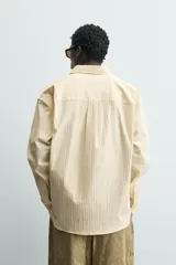 Camisa de corte regular fit confeccionada en tejido de algodón con textura de rayas verticales. Presenta cuello solapa, cierre frontal de botones y mangas largas con puños abotonados.