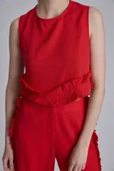 Conjunto de dos piezas color rojo, compuesto por un top sin mangas con detalle de volado fruncido en el bajo y un pantalón ancho de tiro alto con volados largos a lo largo de las costuras laterales exteriores.