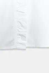 Camisa de color celeste con cuello subido, manga larga abullonada con puños elásticos y detalle de volantes en el cuello y a lo largo de la botonadura frontal.