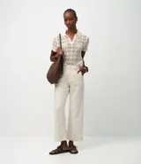 Pantalón de mujer color blanco roto, de corte recto y tiro alto, con un largo cropped y ligero ensanchamiento en el bajo. Presenta detalles bordados florales sutiles en la tela y bolsillos.