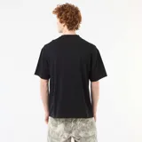Camiseta negra de cuello redondo y manga corta, con bordado frontal en contraste con la inscripción "NXT-K ORIGINAL STREETWEAR APPAREL".