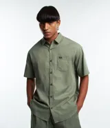 Camisa de corte relajado para hombre, confeccionada en una mezcla de cáñamo y algodón. Presenta cuello inglés, mangas cortas, cierre frontal con botones y un bolsillo de parche en el pecho con una pequeña etiqueta decorativa.