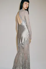 Vestido largo de satén y encaje color gris, con cuello redondo, manga larga y cierre en la espalda con abertura y botón.