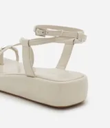 Sandalia tipo flatform color beige, con diseño de tiras finas, dedal metálico en la parte frontal y cierre con hebilla en el talón. Suela plana de altura media.