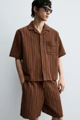 Bermuda de corte relajado color marrón con finas rayas verticales negras. Presenta cintura elástica ajustable con cordón y bolsillos laterales y trasero.