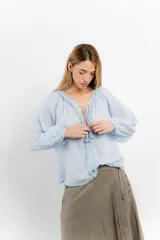 Blusa celeste de algodón con escote en V con lazos y mangas largas abullonadas con puños elásticos.