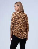 Blusa de seda fría con estampado animal print en tonos marrones. Tiene cuello redondo con escote en V y aro metálico decorativo.