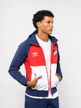 Campera deportiva Umbro del Club Nacional de Football, modelo Summit. Presenta un diseño con bloques de color en azul, rojo y blanco, con capucha, cierre frontal y bolsillos laterales con cierre. Incluye el logo de la marca y el escudo del club en el pecho.