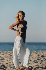 Pantalón de tiro medio confeccionado en tejido satinado blanco, con cintura elástica, diseño plisado y bajo abullonado y asimétrico.