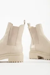 Bota tipo chelsea con suela track de goma en color marrón y capellada de cuero negro. Presenta elásticos laterales y tirador trasero.