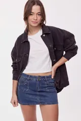 Falda mini de denim azul con calce al cuerpo y tiro medio. Presenta bolsillos delanteros amplios, doble botón en la cintura y aplicaciones de tachas metálicas que recorren la cintura y los bolsillos.