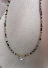 Collar de piedras naturales de turmalina multicolor con cuentas de goldfilled y dije central de cristal tipo punto de luz. Incluye cierre y cadena extensora de acero dorado.