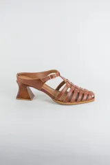 Sandalias de cuero color beige estilo cangrejera con punta fina, diseño de tiras entrelazadas, tira ajustable en el tobillo con hebilla dorada y taco geométrico de madera.