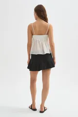 Minifalda de jean negra con diseño cruzado, cierre de hebilla metálica y detalle de tablones plisados en el lateral.