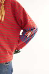 Remera de manga larga con corte boxy, confeccionada en algodón. Presenta un diseño de rayas horizontales en tonos azul y fucsia, con detalles de rayas verticales en los codos, tajos laterales y logo bordado en el pecho.