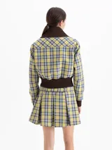 Chaqueta cropped de tela cuadrillé en tonos verde, amarillo y azul. Presenta cuello, puños y ruedo en tejido ribb color chocolate, cierre frontal con cremallera, bolsillos con tapa y detalles en cuero sintético.