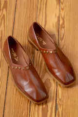 Zapato de cuero vacuno color negro, con punta cuadrada y detalle de tachas metálicas planas en el borde superior. Presenta costura central en el empeine y taco geométrico.