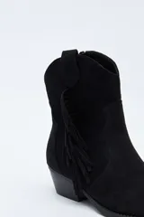 Bota texana de gamuza negra con caña baja, flecos laterales decorativos, costuras estilo western y taco bajo inclinado.