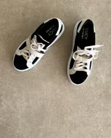 Sneakers de mujer estilo deportivo y urbano, color negro con detalles en beige claro. Presentan puntera y talón en negro, cuerpo principal en negro, y estrella lateral, cordones y tira de velcro en beige claro. La suela es blanca y el interior negro con la inscripción "LUCY IN THE SKY".