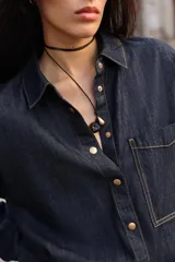 Camisa amplia de denim azul oscuro con cuello solapa, manga larga, bolsillo de plastrón en el pecho y cierre frontal con botones a presión dorados.