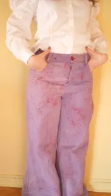 Pantalón de gabardina tiro alto y pierna amplia, teñido a mano con tintes naturales en color violeta con efecto de chispas y salpicaduras. Cuenta con bolsillos delanteros y traseros, presillas para cinto y recortes decorativos en las piernas.