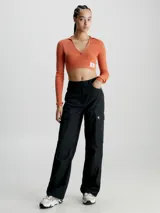 Sweater de punto acanalado color terracota, de manga larga y corte cropped ajustado. Presenta un cuello de chomba con escote en pico profundo y una pequeña etiqueta con el monograma de Calvin Klein en el bajo.