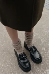 Mocasín de cuero negro con suela gruesa tipo plataforma, detalle de antifaz con aplique metálico dorado y costuras reforzadas en la puntera.