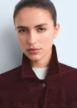 Chaqueta entallada de terciopelo bordó, de manga larga con puños abotonados, cuello camisero, cierre frontal con botones y detalle de costuras visibles.
