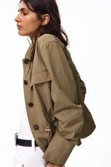 Campera en sarga de algodón color beige, con cuello, cierre frontal con botones ocultos y cordón ajustable en la cintura. Presenta bolsillos de parche con solapa en el pecho y mangas largas.