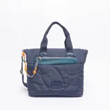 Cartera tipo bolso de mano color azul, con diseño acolchado de formas circulares y orgánicas. Presenta un bolsillo frontal con cierre en color verde petróleo, doble asa superior y una correa lateral decorativa de cuerda trenzada en tonos azul y naranja.