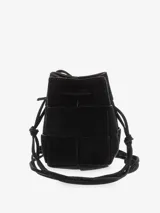 Cartera tipo bucket de gamuza color marrón con diseño trenzado, cierre con lazo ajustable y correa larga para llevar cruzada.