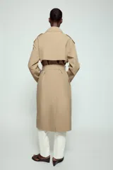 Trench largo de color negro con cuello de solapa, manga larga con trabillas ajustables y cierre frontal cruzado con doble botonadura. Cuenta con bolsillos delanteros de vivo, solapa cortavientos en el pecho y cinturón ajustable del mismo tejido.