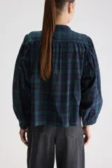 Blusa de calce relajado y silueta amplia, confeccionada en algodón liviano con estampado a cuadros en tonos azul marino y verde. Presenta cuello mao, cierre frontal con botones, hombros fruncidos y mangas largas con volumen que finalizan en puños elastizados.