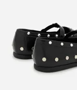 Zapato tipo salomé de color negro con acabado liso, puntera redondeada y suela plana. Presenta una tira central con hebilla metálica ajustable y está decorado con tachuelas metálicas plateadas distribuidas por toda la superficie.