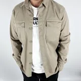 Sobrecamisa beige de gabardina con cuello clásico, cierre frontal con botones a tono, dos bolsillos de parche en el pecho con solapa y manga larga con puños abotonados.