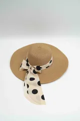 Sombrero de ala ancha confeccionado en fibra natural, con cinta decorativa de tela en color crema con estampado de lunares negros y detalle de lazo lateral.