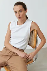 Musculosa blanca de cuello redondo, con detalle de botones decorativos en los hombros y sisas amplias.