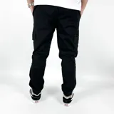 Pantalón cargo negro de gabardina, corte ajustado con puños elásticos en los tobillos. Presenta bolsillos laterales tipo parche con solapa y un pequeño parche de cuero marrón en uno de ellos.