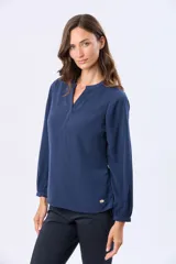Blusa de manga larga en color azul marino, con escote en V y diseño de doble capa en el frente. Presenta puños elásticos y un pequeño aplique metálico decorativo en el ruedo.