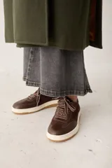 Zapatillas de cuero con textura de pelo, color marrón, con suela de goma color crema y cordones gruesos con diseño trenzado.