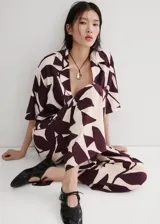 Pantalón largo de corte recto y tiro alto, con estampado abstracto en tonos bordó y crudo. Cuenta con cintura ajustable con elástico y un lazo incorporado para anudar.