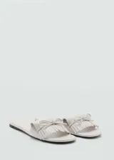 Sandalia plana tipo chinela color blanco, con diseño destalonado y tira frontal decorada con flecos y un pequeño lazo central.