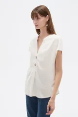 Blusa de viscosa color blanco, de corte holgado, con cuello en V y cierre frontal parcial de botones grandes con efecto carey.