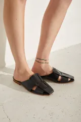 Zueco de cuero color negro, de diseño plano con punta cuadrada y tiras anchas entrelazadas en el empeine.