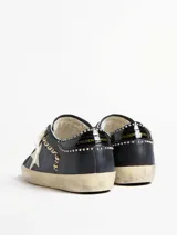 Zapatilla Golden Goose modelo Super-Star de estilo urbano con efecto desgastado. Presenta cuerpo de cuero blanco, estrella lateral con glitter plateado, talón en tono gris texturizado y forro interior de corderito sintético.