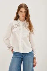 Camisa negra de algodón con detalles de encaje calado en el pecho, hombros y puños. Presenta cuello alto con terminación de encaje, cierre frontal con botones y mangas largas abullonadas.